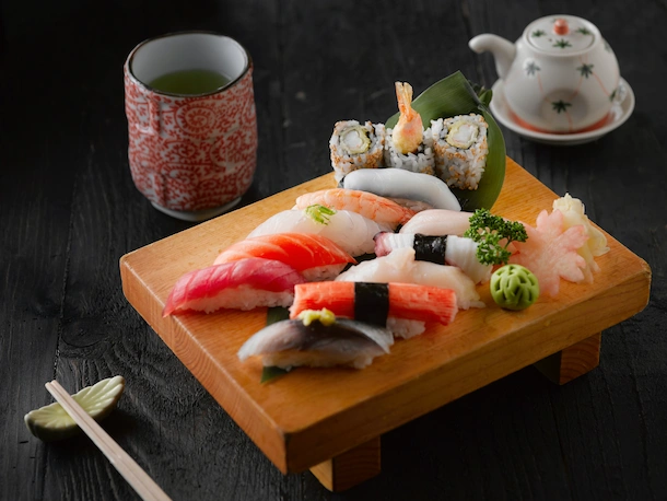 Sushi on display on a brown wood board, served with green tea