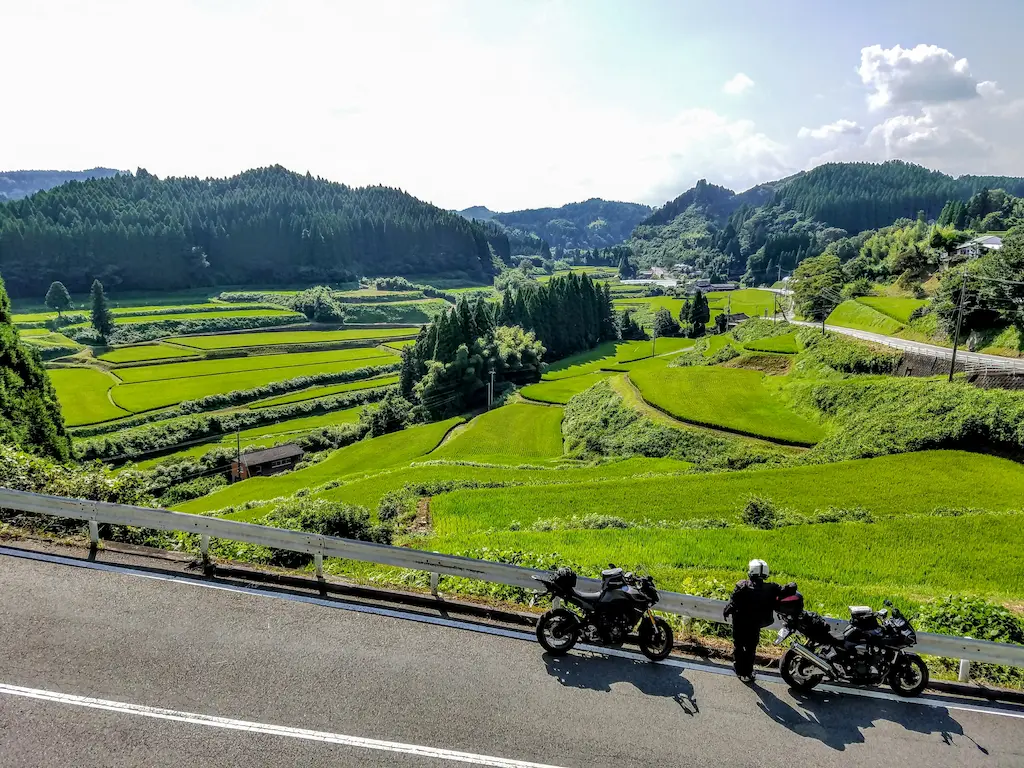 Two motorcylces parked along the side of a country road overlooking terraced rice fields.