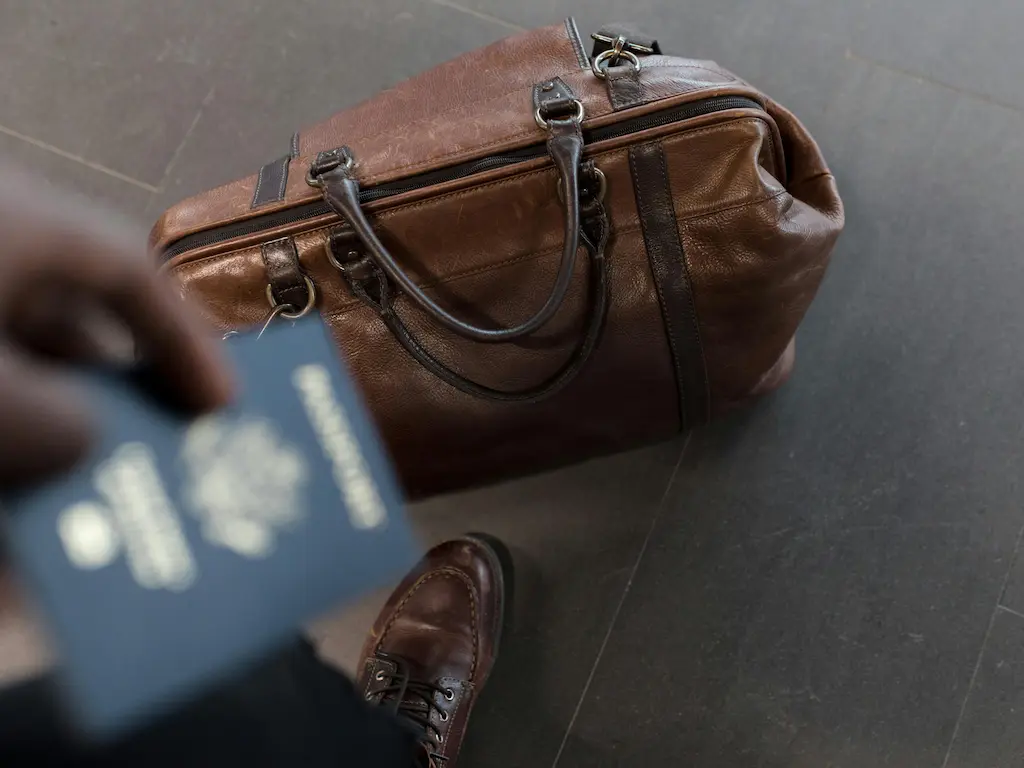 A man's luggage laying at the feet of a man holding his US Passport